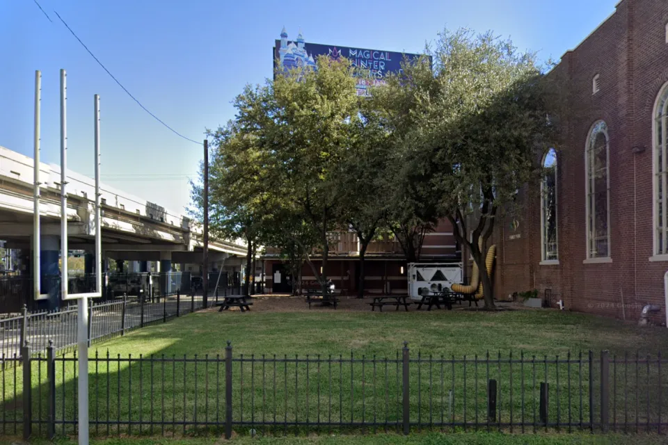 Google street view of grassy lot next to brick church with elevated freeway on other side in Houston, Texas.
